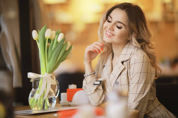 girl sitting in a cafe at a table / beautiful young model posing with a bunch of flowers, happy adult girlfriend - Foto, Imagen