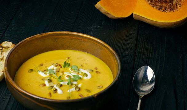 Pumpkin soup in a bowl with cream and pumpkin seeds. Vegan soup. Dark wooden background. - Valokuva, kuva