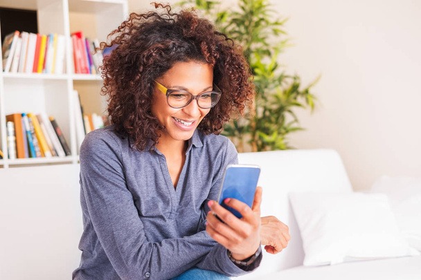 Социальные сети. Молодая черная женщина отправляет сообщения на смартфон дома
 - Фото, изображение