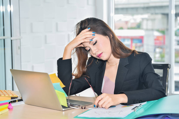 Mujer de negocios estresada sentada y sosteniendo la cabeza debido al dolor de cabeza en la oficina moderna
 - Foto, Imagen