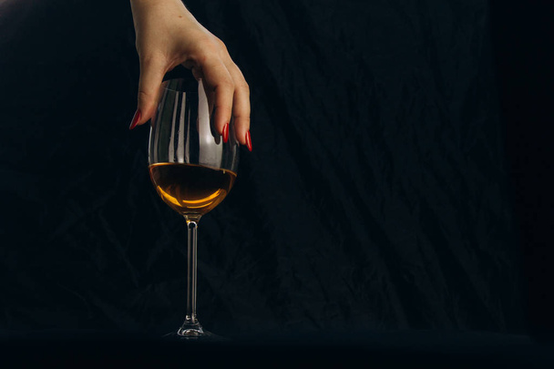 cropped female hand holding a glass of white wine on a black background. rest, holiday, party. isolated alcoholic drink closeup. - Фото, изображение