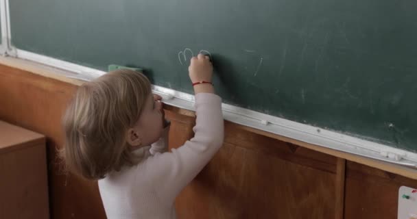 Dívka, která kresní na tabuli pomocí křídy ve třídě. Proces vzdělávání - Záběry, video