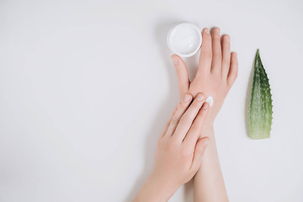 Beautiful groomed woman's hands with organic cream jar and Aloe vera fresh leaves on white background. Moisturizing cream for clean and soft skin. Flat lay, top view, copy space. Healthcare concept. - Photo, Image