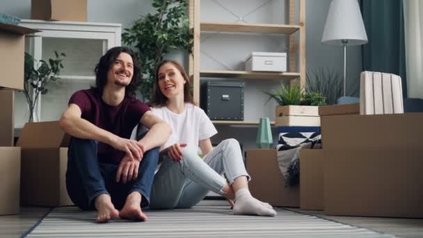 Genç çift konuşmak ve öpüşme oturma üzerinde zemin ile kutular hareket içinde yeni düz - Video, Çekim