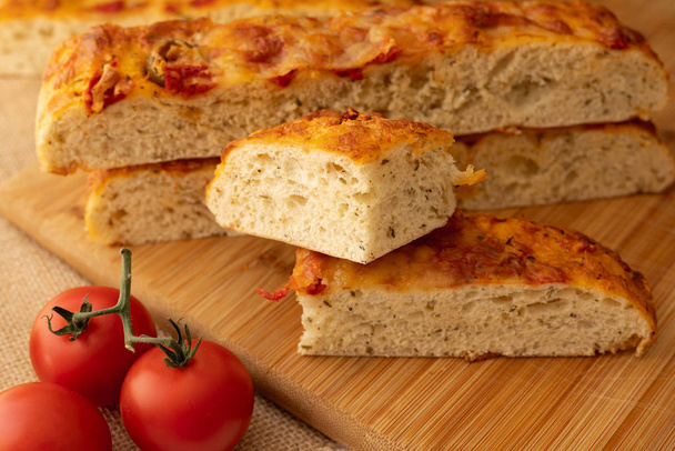 Focaccia, italský domácí chléb a rajčata zavřete na dřevěné sekací desce - Fotografie, Obrázek