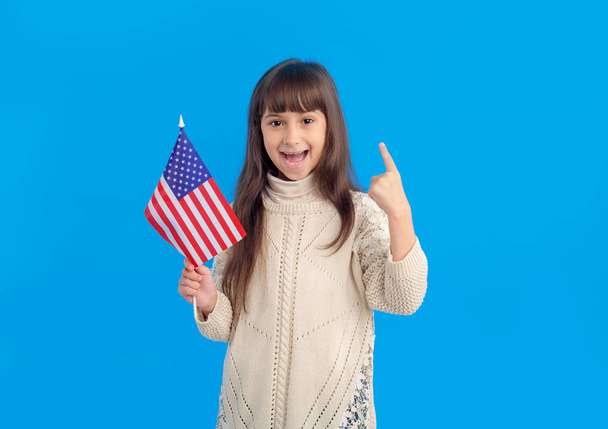 Little happy girl with USA flag shows one finger points upwards on a blue background. - Foto, imagen