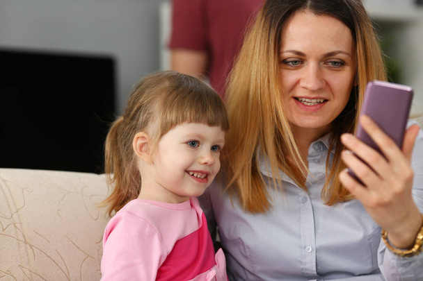 Mother and her baby girl daughter using cellphone for calling siblings - Zdjęcie, obraz