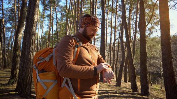 Be on time in travel and adventures. Waist up portrait of bearded man traveler, with backpack, uses technology sports watch for navigating gps electronic compass in forest and looking at his watch - Photo, Image