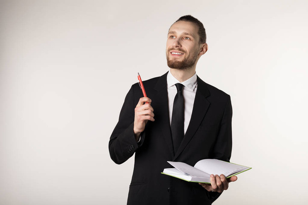 junge attraktive bärtige Lehrerin in schwarzem Anzug und Krawatte mit Notizbuch und Stift in der Hand - Foto, Bild