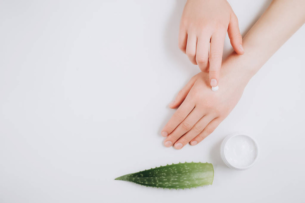 Beautiful groomed woman's hands with organic cream jar and Aloe vera fresh leaves on white background. Moisturizing cream for clean and soft skin. Flat lay, top view, copy space. Healthcare concept. - Fotoğraf, Görsel