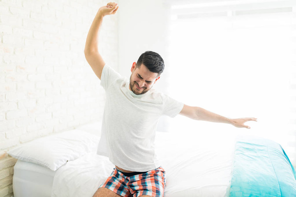 Giovane uomo in biancheria da notte svegliarsi al mattino e stretching sul letto
 - Foto, immagini