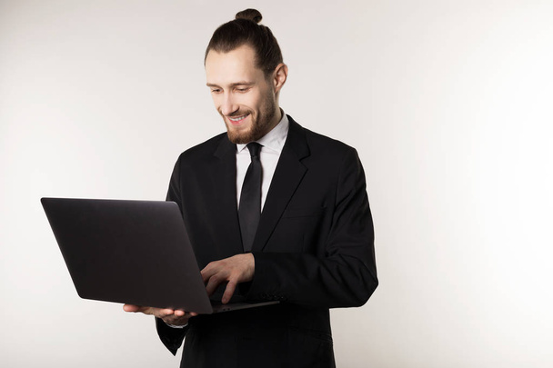 Νέος όμορφος επιχειρηματίας με γένια και μοντέρνα χτένισμα φορώντας μαύρο κοστούμι και γραβάτα - Φωτογραφία, εικόνα