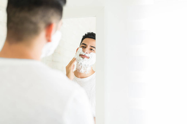 Bom olhar jovem colocando creme de barbear em seu rosto no banheiro
 - Foto, Imagem