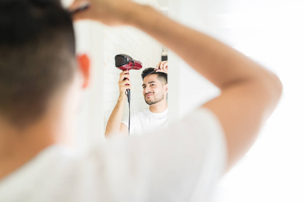 Hispanic good looking man making hairstyle with hairdryer and brush - 写真・画像