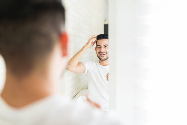 Spokojený mladý muž, který si v koupelnovém zrcadle prověřil svůj nový účes - Fotografie, Obrázek