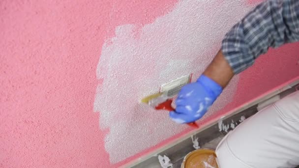 Ein kaukasischer Maler in weißen Overalls streicht mit dem kleinen Pinsel die rosa Wand mit weißer Farbe an. Bauwirtschaft. Bildmaterial. - Filmmaterial, Video