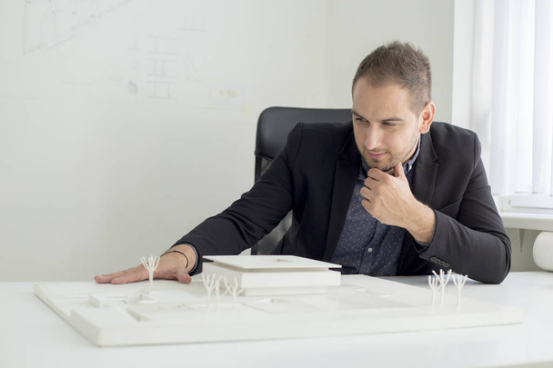 Empresário no escritório está olhando de perto para a arquitetura de um modelo de casa moderna
 - Foto, Imagem