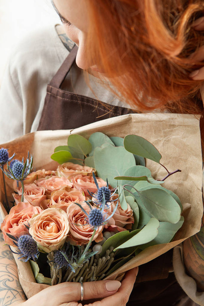 Happy female with ginger hair holds beautiful bouquet of roses living coral colored and eryngium. Gift for Mother's Day or Woman's Day. Close up. - Fotografie, Obrázek