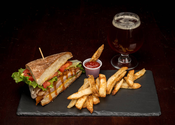Copo de cerveja chique com meia sanduíche de clube com batatas fritas
 - Foto, Imagem