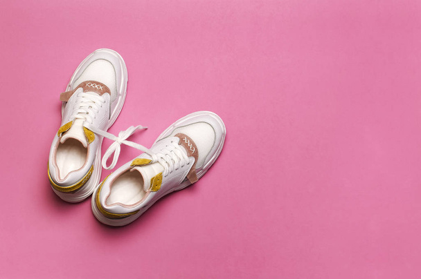 Witte vrouwelijke sneakers op heldere roze achtergrond. Fashion blog of magazine concept. Damesschoenen, trendy Sneakers, mode, stijl, lifestyle. Platte lay bovenaanzicht kopie ruimte minimale achtergrond. - Foto, afbeelding