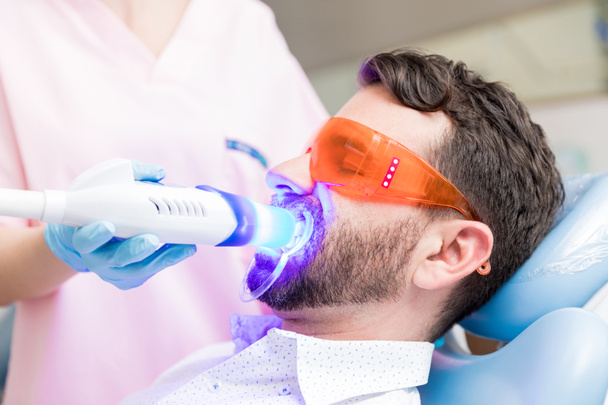 Closeup of man undergoing laser tooth whitening treatment to remove stains and discoloration - Foto, Bild