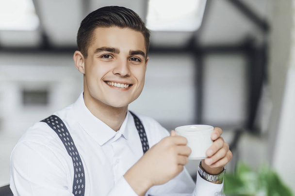 Young stylish businessman drinking cup of coffee at office - Foto, afbeelding