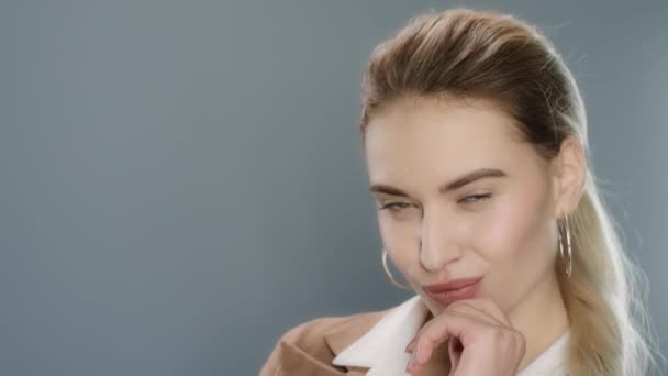 Αισθησιακή γυναίκα που ποζάρει και κλείνει το μάτι στην κάμερα σε γκρι φόντο στούντιο - Πλάνα, βίντεο