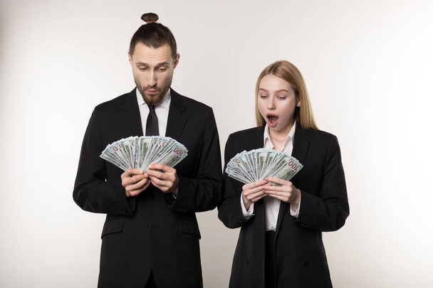 Portrait of couple in black suits shocked holding money banknotes in hands - Фото, зображення
