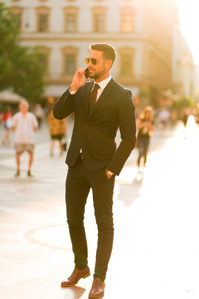 Een zakenman die loopt en praat op zijn telefoon. - Foto, afbeelding