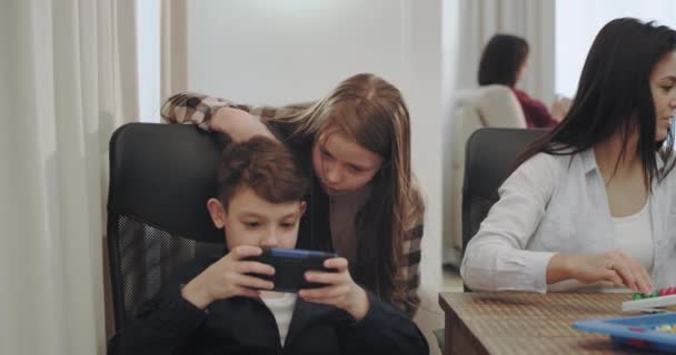 Gyönyörű érett anya kiadási időt vele három gyermeke, játékasztal játékok két gyerek játszik a smartphone, háttérben nagyi olvas egy könyvet. - Felvétel, videó