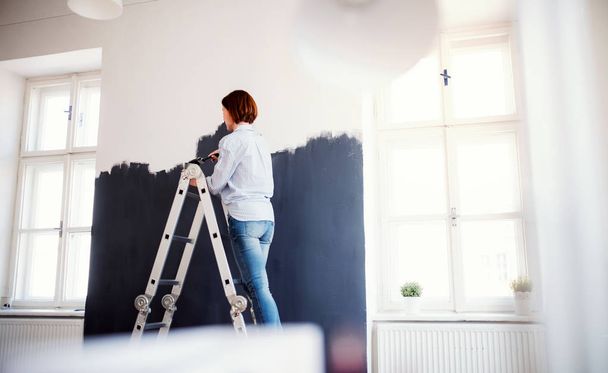 A young woman painting wall black. A startup of small business. - Фото, зображення