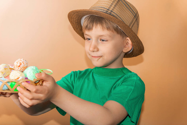 Een jongen in een strohoed houdt geschilderde paaseieren in zijn hand. - Foto, afbeelding