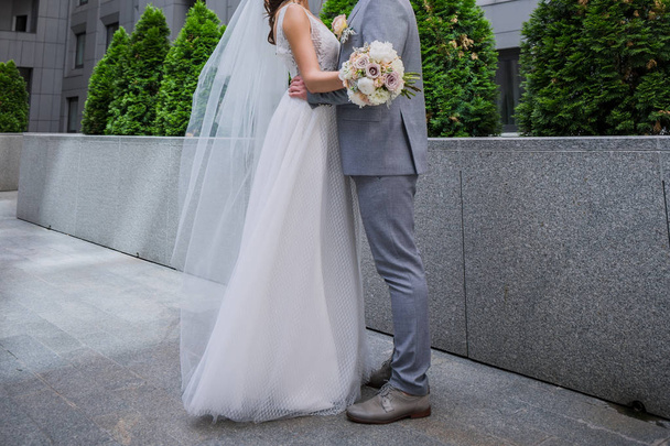 The bride and groom are standing together near the office building. - 写真・画像