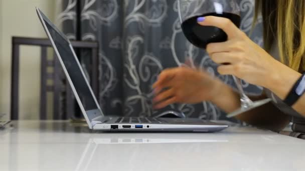 holding a glass of wine in her right hand, the girl with her left hand is typing on a laptop - Filmmaterial, Video