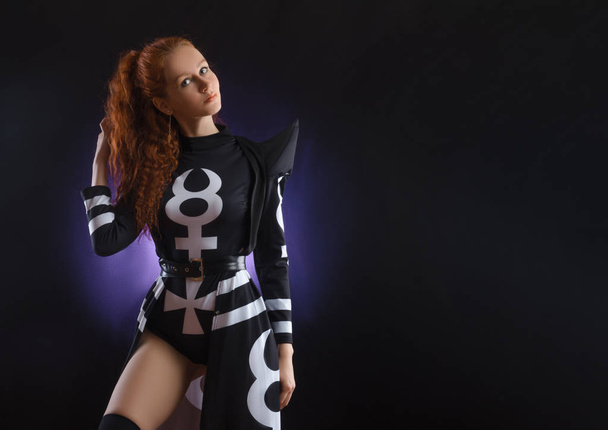 red-haired girl in an unusual suit posing on a black background - Photo, Image