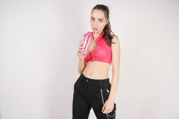 young beautiful caucasian teen girl in a pink short topic with a glass of water after training on a white background in the Studio - Φωτογραφία, εικόνα