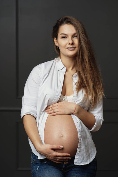 Linda jovem grávida tocando suavemente com as mãos sua barriga, enviando amor para seu bebê por nascer
 - Foto, Imagem