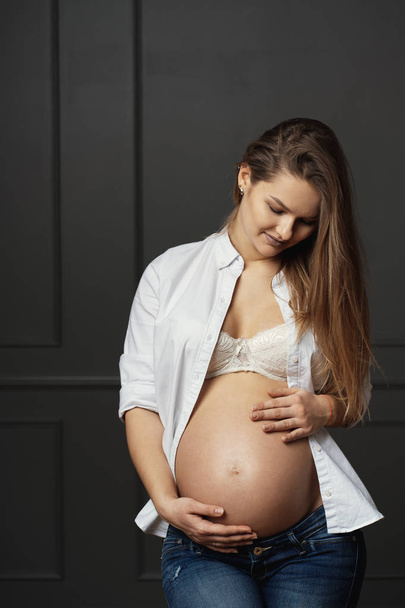Krásná mladá těhotná žena se jemně dotýkala svého břicha a posílá lásku k jejímu nenarozené dítěti - Fotografie, Obrázek