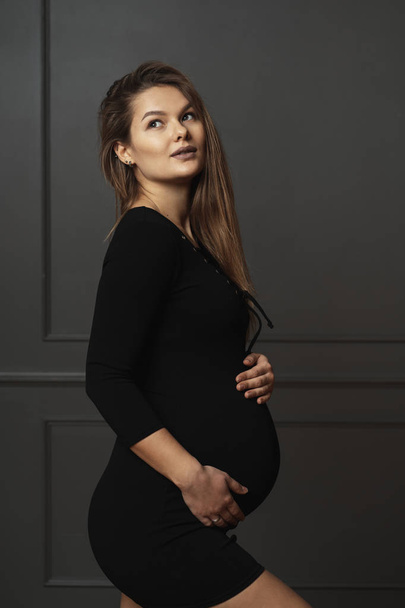 Porträt wunderschöne junge schwangere Frau berührt sanft mit den Händen ihren Bauch, sie wartet auf ein neues Leben - Foto, Bild