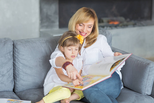 Mother and little daughter are playing, reading a book, sitting  - Photo, image
