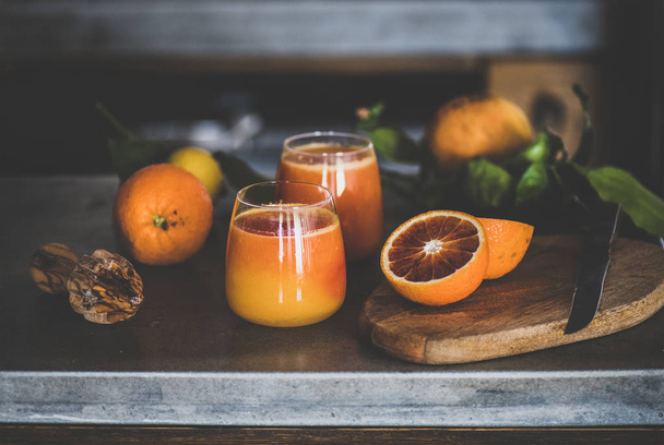 Glasses of freshly squeezed blood orange juice or smoothie on concrete kitchen counter. Healthy lifestyle, vegan, vegetarian, alkaline diet, spring detox concept - Photo, image