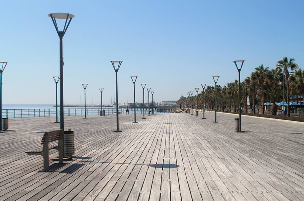 Limassol, Cyprus, March 22nd, 2019: Wooden sea pier on Molos promenade with walking and sitting people, street lights and benches on a sunny day - Фото, изображение