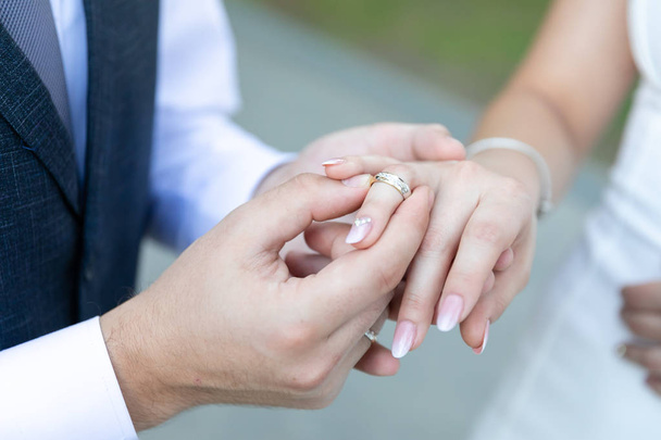 A man in a vest and tie wearing a gold wedding ring to a woman in a wedding dress on the ring finger. - Foto, afbeelding