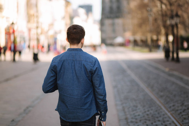 Вид сзади на человека, идущего по центру города. Синяя рубашка
 - Фото, изображение