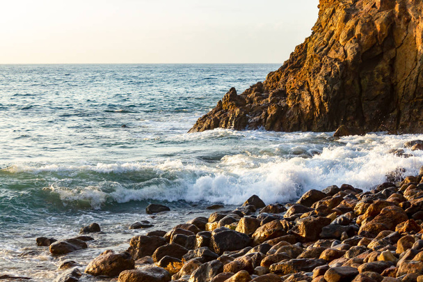 волна, разбивающаяся о скалы на берегу с восходом солнца
  - Фото, изображение