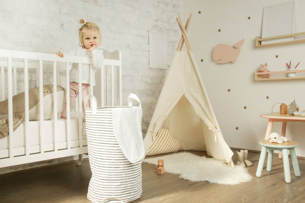 Adorable cheerful baby girl in the crib in the nursery room - 写真・画像