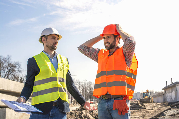 男性、エンジニア、ヘルメットの労働者は、建設現場で彼らの上司と一緒に、図面、修理を見ている - 写真・画像