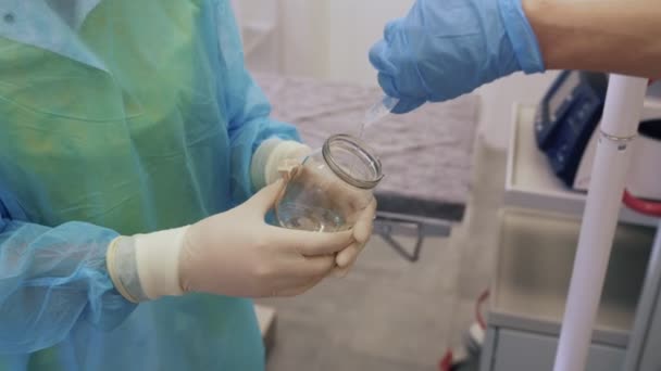 Zbliżenie rąk lekarza wylewa środek dezynfekcyjny do szklanego słoika w posiadaniu pielęgniarki - Materiał filmowy, wideo