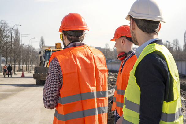 ingenieros trabajadores masculinos en un sitio de construcción con la cabeza en cascos mirar a la casa que se está construyendo
 - Foto, imagen