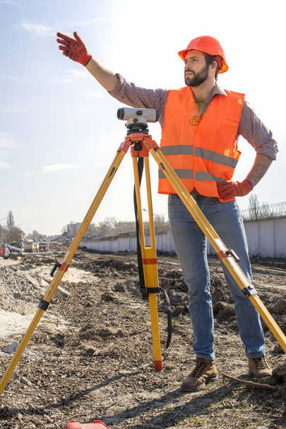 mannelijke Surveyor Engineer met een apparaat dat werkt op een bouwplaats in een helm - Foto, afbeelding
